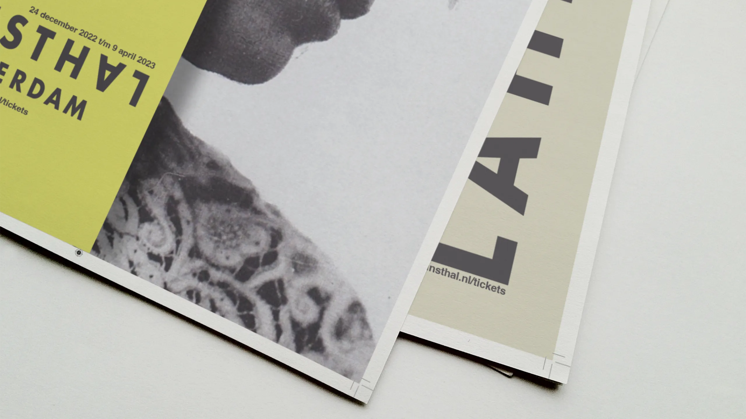 Two Kunsthal Rotterdam exhibition posters fanned at close range — the bold yellow version and the cream version, both showing fragments of typography and portrait at the edge of print