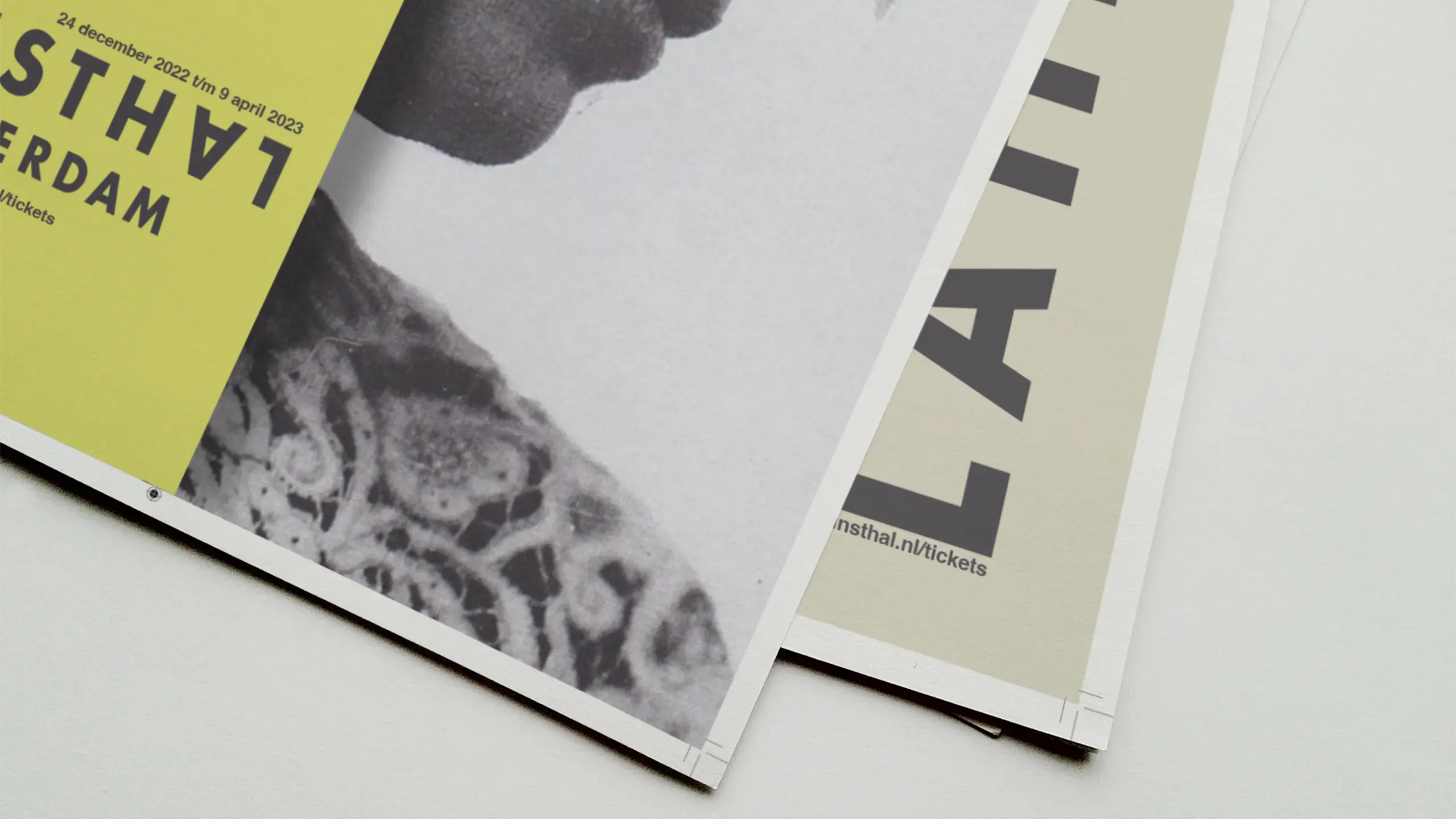 Two Kunsthal Rotterdam exhibition posters fanned at close range — the bold yellow version and the cream version, both showing fragments of typography and portrait at the edge of print